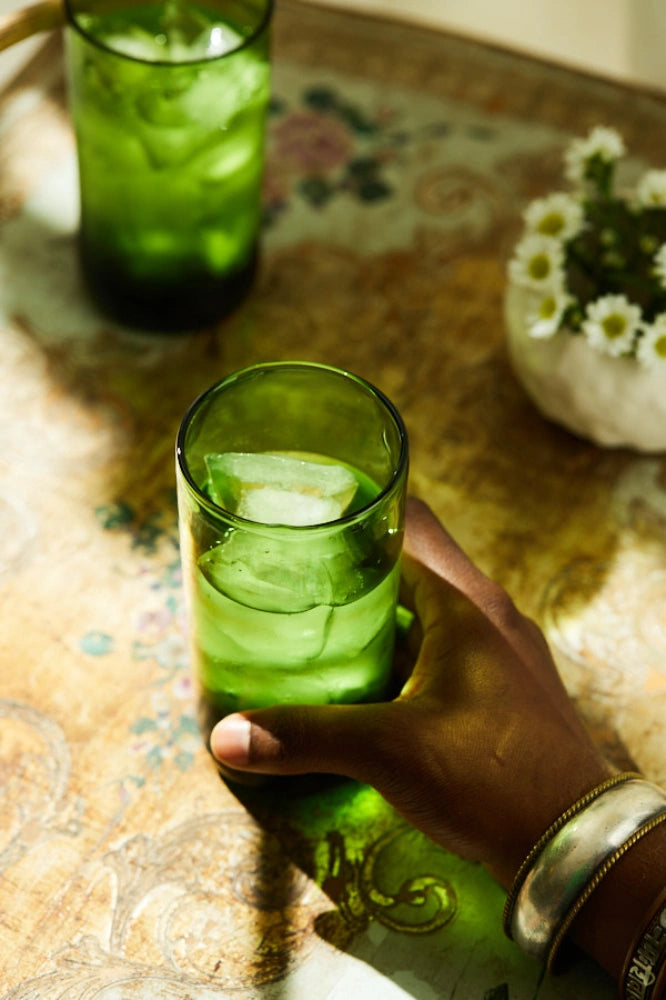 Green deep tinted tall highball glass, filled with water, placed on a table in a summer party setup, made from 100% recycled glass.