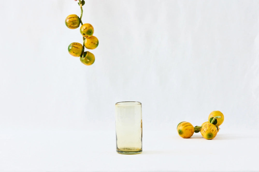 Amber yellow lightly tinted tall highball glass, made from 100% recycled glass, shown from the side on a white background.