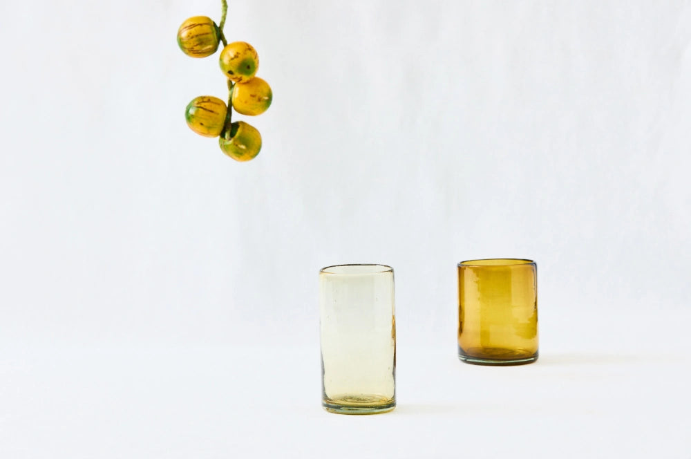 A tall and short amber yellow drinking glass, lightly tinted, made from 100% recycled glass, displayed together on a white background.