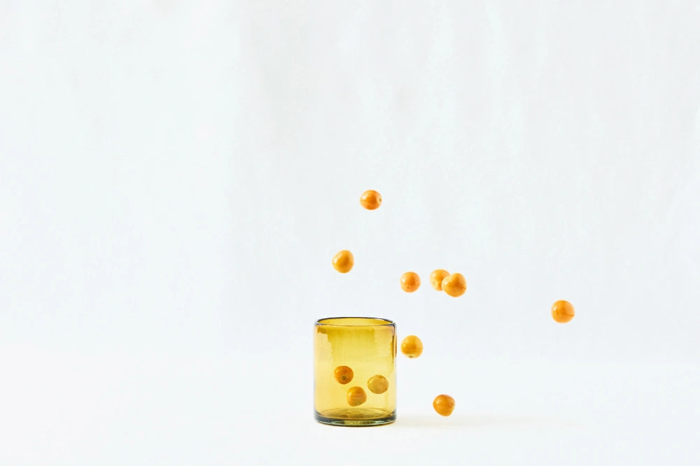 Amber lightly tinted short glass tumbler, made from 100% recycled glass, shown from the side on a white background.