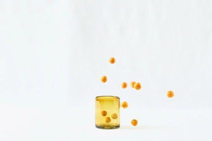 Amber lightly tinted short glass tumbler, made from 100% recycled glass, shown from the side on a white background.