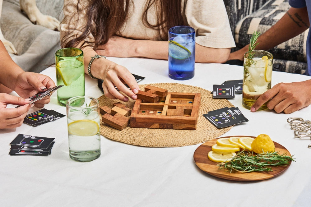 Four lightly tinted tall highball glasses, in clear, blue, green and yellow glass, arranged for summer drinks in a housewarming party setting, made from 100% recycled glass.