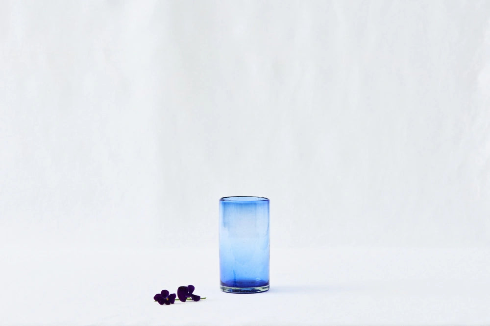 Blue lightly tinted tall highball glass, made from 100% recycled glass, shown from the side on a white background.