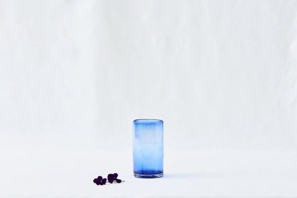 Blue lightly tinted tall highball glass, made from 100% recycled glass, shown from the side on a white background.