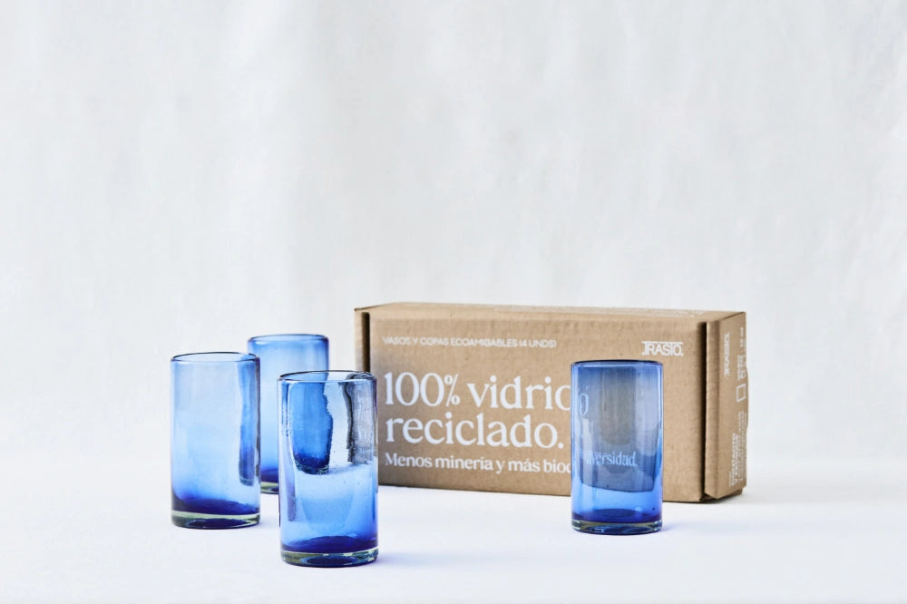 Four blue lightly tinted tall highball glasses, made from 100% recycled glass, shown side by side with packaging on a white background.