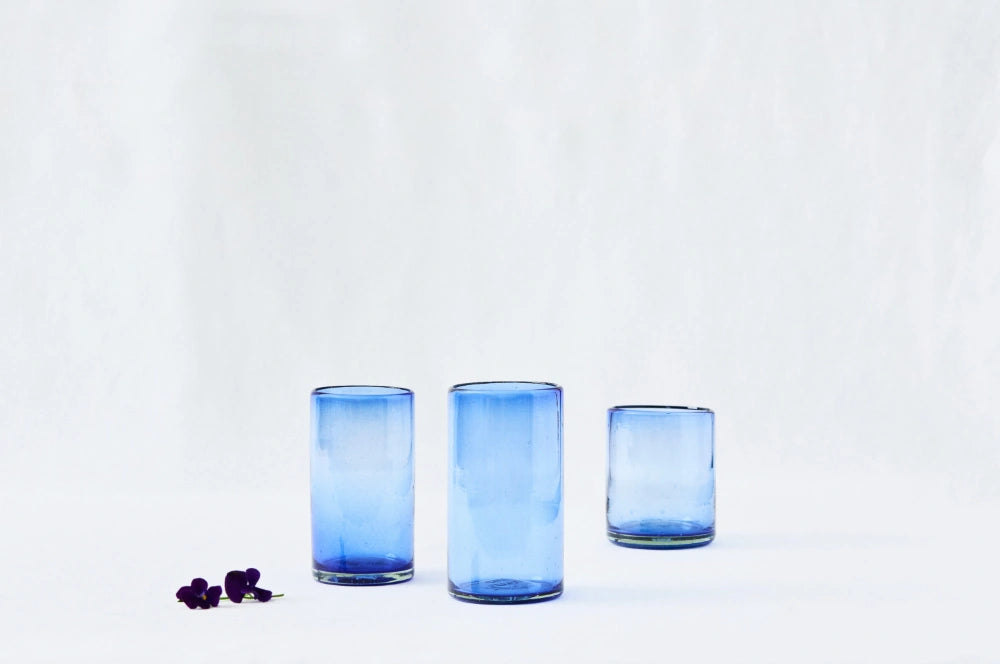 Short, tall, and large everyday blue lightly tinted drinking glasses, made from 100% recycled glass, displayed side by side on a white background.