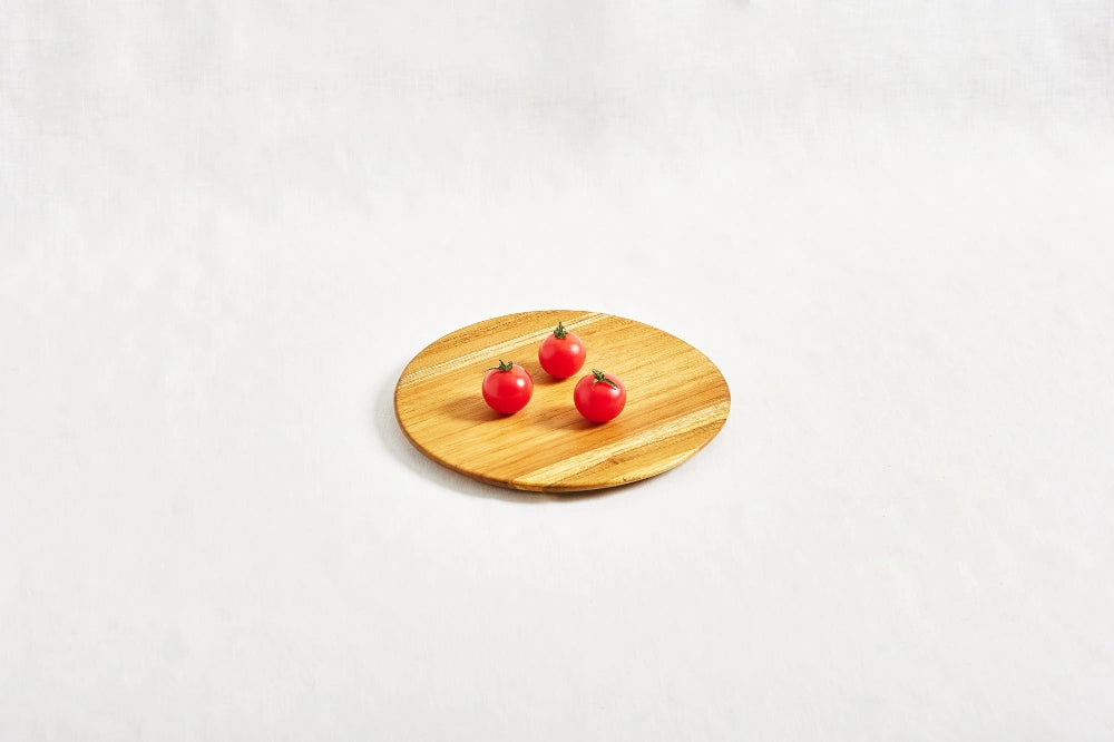 One small round appetizer tray made from 100% certified teak wood, with three cherry tomatoes placed on top, displayed on a white background.