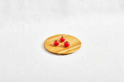 One small round appetizer tray made from 100% certified teak wood, with three cherry tomatoes placed on top, displayed on a white background.