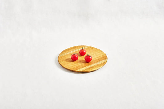 One small round appetizer tray made from 100% certified teak wood, with three cherry tomatoes placed on top, displayed on a white background.