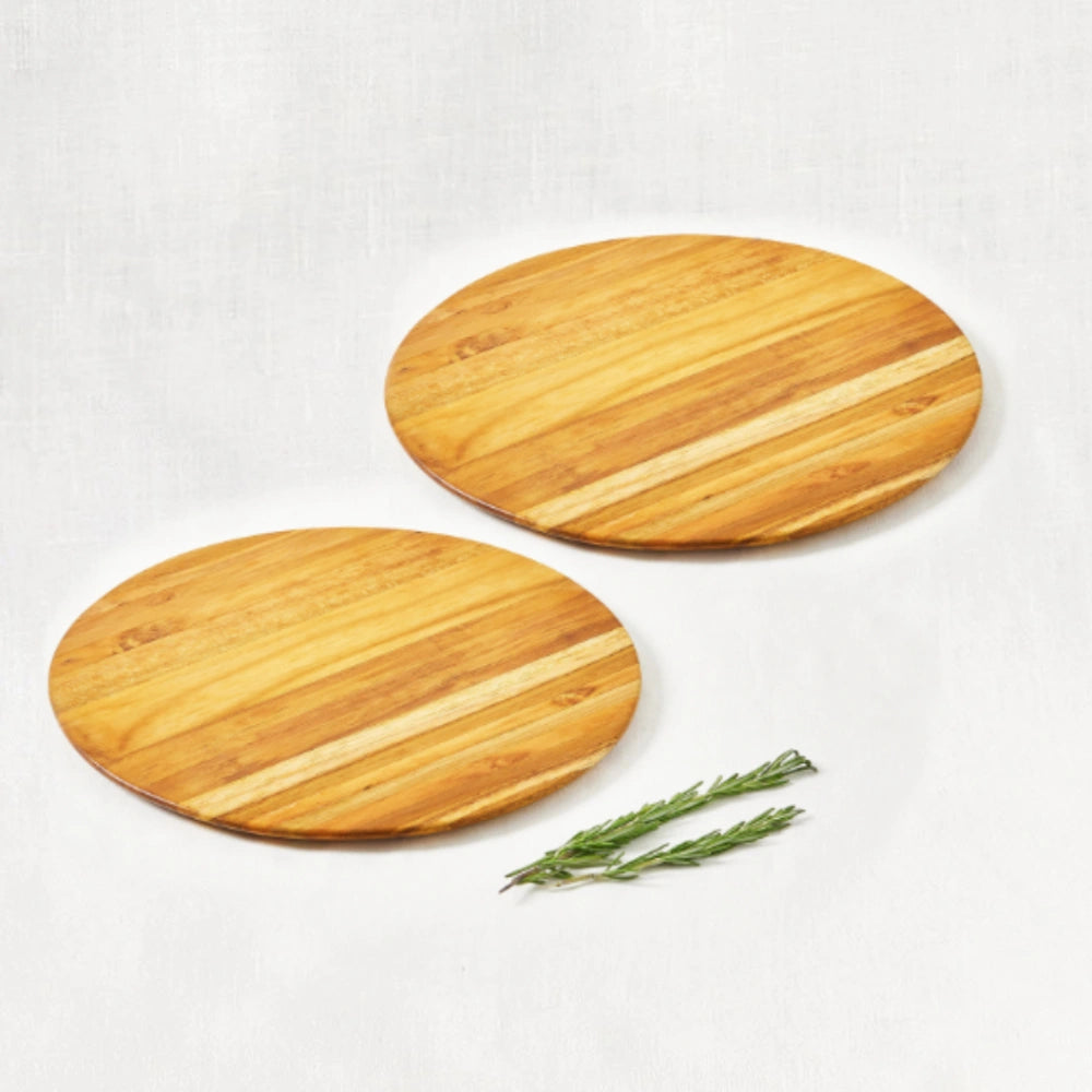 Two large round teak wood boards for pizza, bread, appetizers, or cheeses, displayed on a white background with a sprig of rosemary and a short turquoise bowl placed next to them.