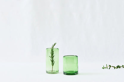 A tall and short green drinking glass, lightly tinted, made from 100% recycled glass, displayed together on a white background.