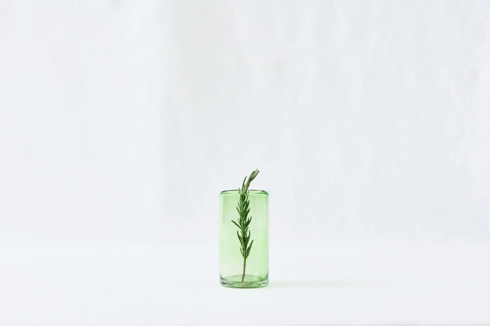 Green lightly tinted tall highball glass, made from 100% recycled glass, shown from the side on a white background.