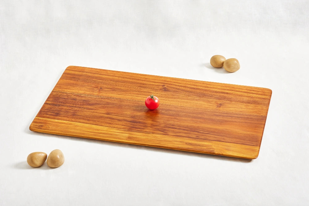 One large super lightweight cutting board made from 100% certified teak wood, featuring a beveled edge, with a cherry tomato placed on top to show scale, displayed on a white background.