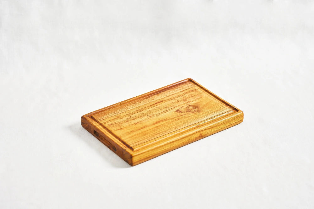 One small premium reversible teak cutting board showcasing a juice groove, lying flat on a white background at a diagonal angle, highlighting its smooth surface and dual-use design, made from 100% certified teak wood.