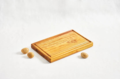 One small premium reversible teak cutting board showcasing a juice groove, lying flat on a white background at a diagonal angle, highlighting its smooth surface and dual-use design, made from 100% certified teak wood.