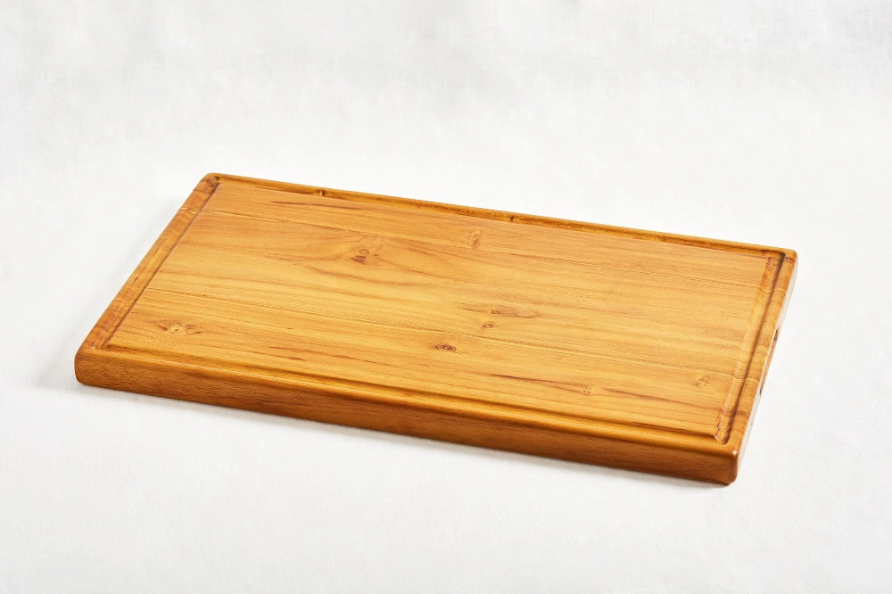 One large premium teak cutting board featuring a handle and juice groove, lying flat at a diagonal angle on a white background, showcasing its smooth surface and craftsmanship, made from 100% certified teak wood.