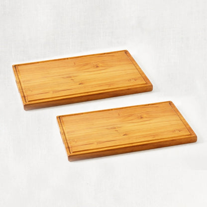 Two large premium teak cutting boards featuring integrated handles and juice grooves, lying flat in a diagonal perspective against a white background, showcasing their smooth surfaces and craftsmanship.