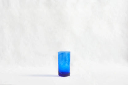 Blue deep tinted tall highball glass, made from 100% recycled glass, shown from the side on a white background.