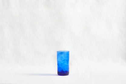 Blue deep tinted tall highball glass, made from 100% recycled glass, shown from the side on a white background.