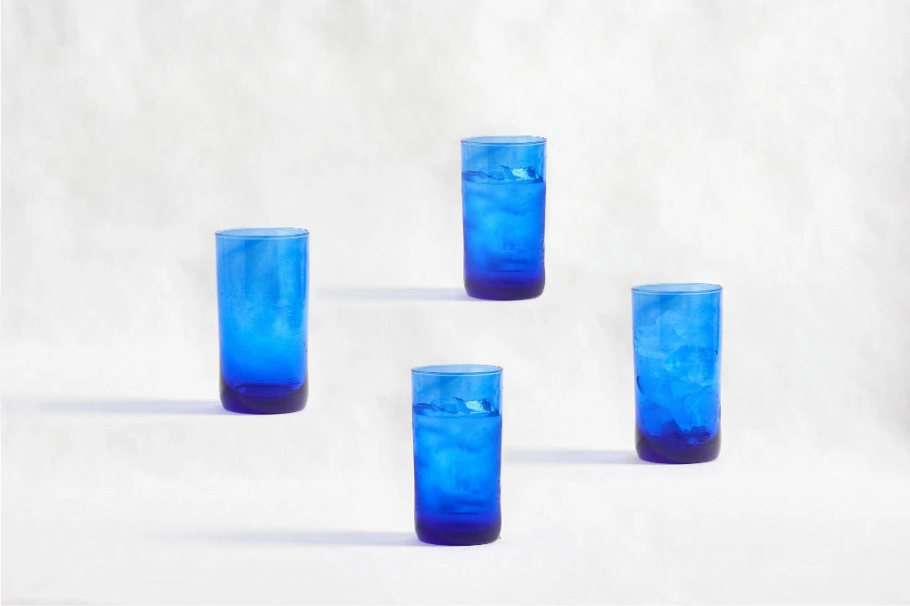 Four blue deep tinted tall highball glasses, made from 100% recycled glass, arranged together on a white background.