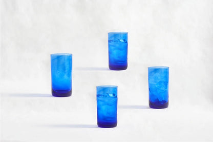 Four blue deep tinted tall highball glasses, made from 100% recycled glass, arranged together on a white background.