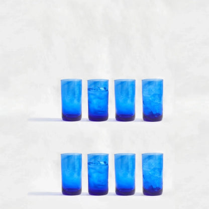 Eight blue deep tinted tall highball glasses, made from 100% recycled glass, arranged together on a white background.