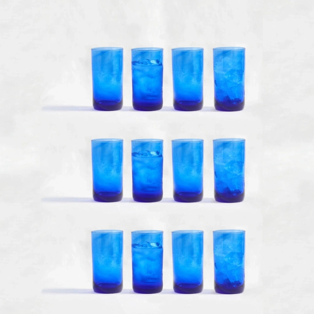 Twelve blue deep tinted tall highball glasses, made from 100% recycled glass, arranged together on a white background.