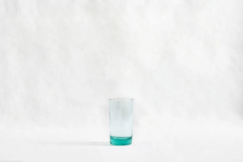 Turquoise tall highball glass, made from 100% recycled glass, shown from the side on a white background