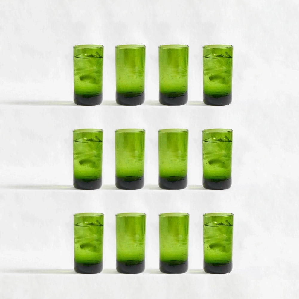 Twelve green deep tinted tall highball glasses, made from 100% recycled glass, arranged together on a white background.