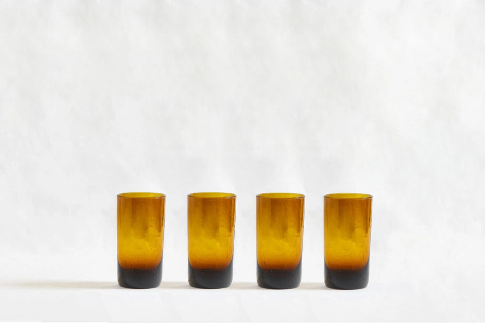 Four amber deep tinted tall highball glasses, made from 100% recycled glass, arranged together on a white background.