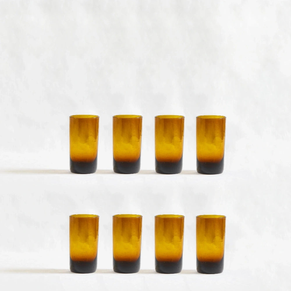 Eight amber deep tinted tall highball glasses, made from 100% recycled glass, arranged together on a white background.