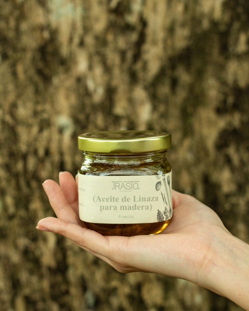 100% pure raw linseed oil for wood finishes and kitchen board maintenance, packaged in a 6-ounce glass jar with a metal cap, displayed against the trunk of a tree.