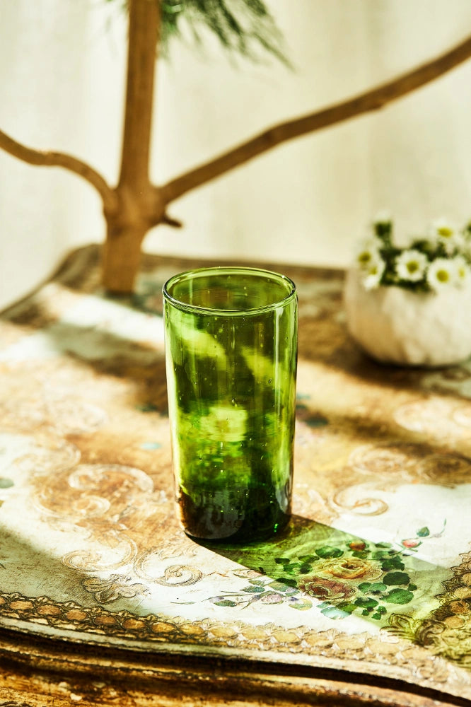 Deep tinted tall highball glass, placed on a table in a summer party setup, made from 100% recycled glass.