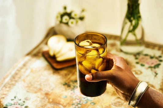 Amber deep tinted tall highball glass, filled with water, placed on a table in a summer party setup, made from 100% recycled glass.