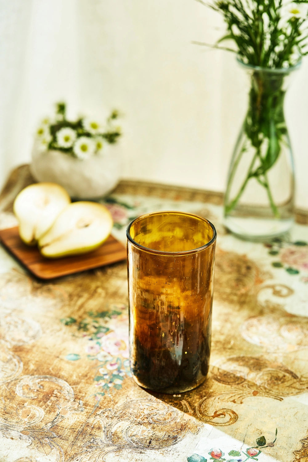 Amber deep tinted tall highball glass, placed on a table in a summer party setup, made from 100% recycled glass.